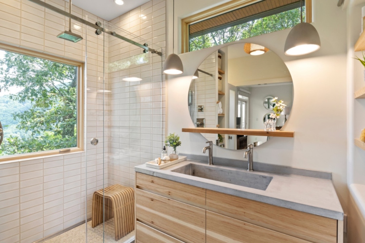  Kupatilo opremljeno u skandinavskom stilu sa drvenim ormarićima i okruglim ogledalom